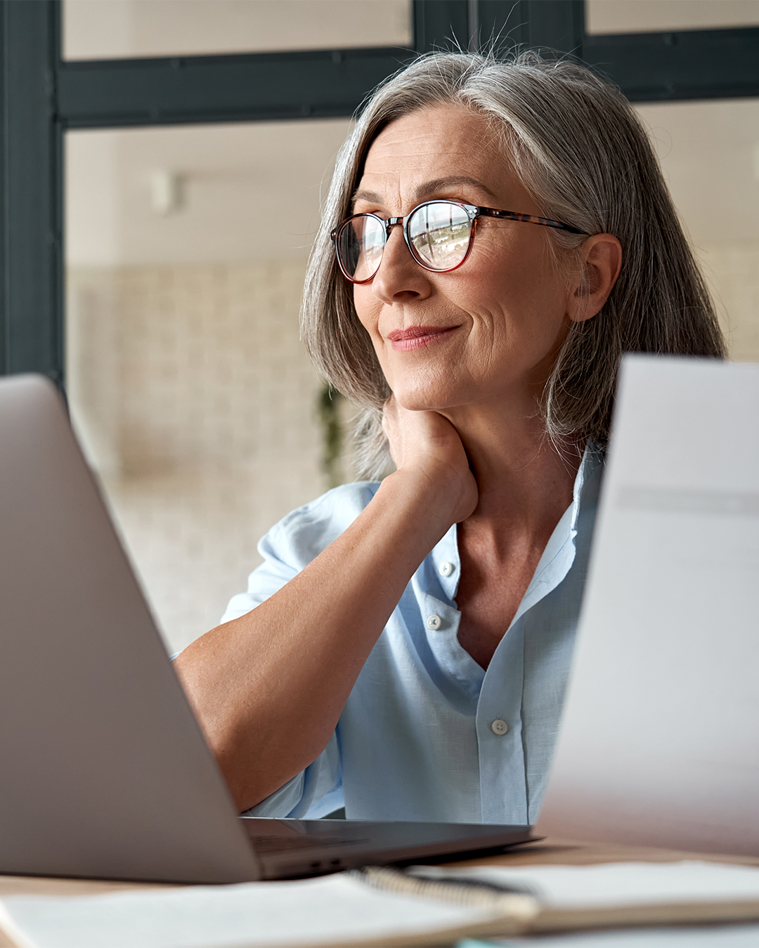 Woman holds paper while looking at laptop