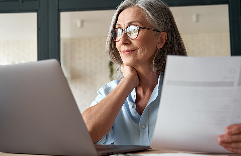 Woman holds paper while looking at laptop