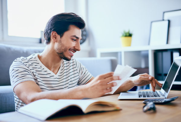 Man smiling while holding receipts and looking at laptop