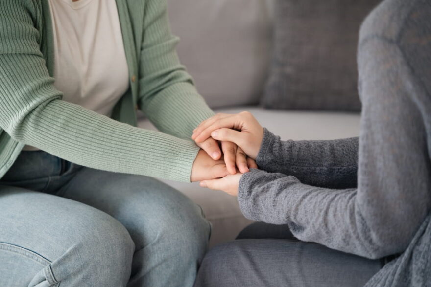 sisters sitting down and holding hands after death of family member